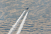 Flugzeug mit Kondensstreifen über Wolkendecke