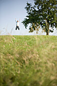 Junger springt in die Höhe auf einer Wiese