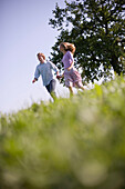 Couple running down on meadow holding hands