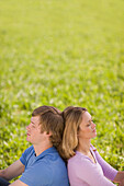 Couple sitting back to back on meadow