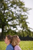 Couple sitting back to back on meadow