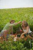 Couple having picnic on meadow, man feeding woman grapes
