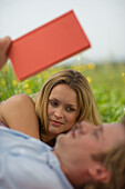 Junges Paar liegt im Gras, Mann liest ein Buch
