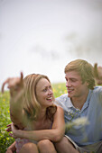 Young couple sitting on meadow, both pointing