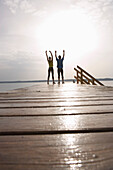 Two people standing on jetty, arms raised
