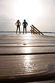 Two people standing on jetty, with hands on hips