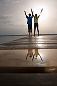 Two people standing on jetty, arms raised