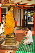 Women praying in front of gilded Buddha statue, Wat Intharawihan, Banglamphu, Bangkok, Thailand