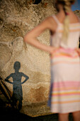 Rear view of a girl standing with her hand on her hip, shadow falling on rock,Santa Giulia Beach, Southern Corse, France