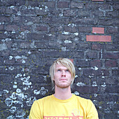Pensive blond young man leaning against brick wall