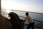 Ein Mann räumt bei Sonnenuntergang das Deck auf, Kreuzfahrtschiff MS Delphin Renaissance