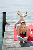 Woman reading a book on jetty, lying on front, Starnberger See, Upper Bavaria, Germany