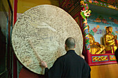 Monk standing in front of a gong, Wannian monastery, Emei Shan, Sichuan province, China, Asia