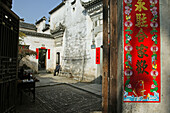 Ein Mann sitzt vor dem Eingang eines traditionellen Hauses in der Sonne, Hongcun, Huangshan, China, Asien