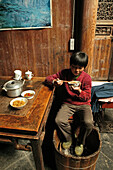 A boy eating and warming his feet at a foot warmer, Hongcun, Huang Shan, China, Asia