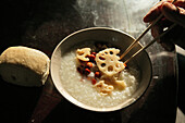 Vegetarische Reissuppe mit Lotuswurzel, Hand hält Stäbchen, Chinesische Mahlzeit, China, Asien