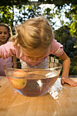 Mädchen beugt sich über eine Schüssel mit Wasser und einen Apfel, Kindergeburtstag