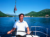 Mann am Steuerad eines Segelboots auf der Adria, Dalmatien, Kroatien