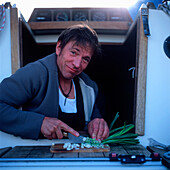 Man standing on a sailboat cutting shallots, portrait, Bay of Kiel between Germany and Denmark
