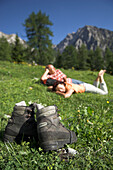 A couple lying in a meadow after a hiking tour, with hiking boots in the foreground, Hengstpass, Austria