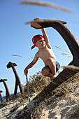 Boy playing pirate at a rosty anchor on beach, Ilha de Tavira, Tavira, Algarve, Portugal