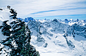 Freerider stehen oben an einer Felswand und schauen in eine wilde Berglandschaft hinaus. Dome de la Lauze, La Grave Oisans, Parc National des Ecrins, Frankreich, Alpen