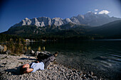 Mann entspannt sich am Ufer, Eibsee, Zugspitze im Hintergrund, Bayern, Deutschland