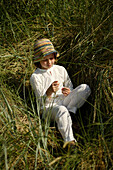 Girl sitting on beach grass and playing with a blade of grass, Travemuende Bay, Schleswig-Holstein, Germany