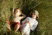 Girl and boy lying on beach grass, Travemuende Bay, Schleswig-Holstein, Germany