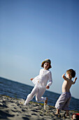 Girl running over Baltic Sea beach, boy blockading the way, Travemuende Bay, Schleswig-Holstein, Germany