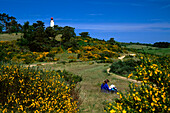 Woman resting on grass, lighthouse in background, Hiddensee Island, Mecklenburg-Western Pomerania, Germany