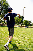 Ein junger Mann wirft einen Ball auf einer Wiese, The National Mall, Washington DC, Amerika, USA