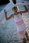 Girl (6-7 years) walking over beach, carrying inflatable toy plane, Santa Giulia, Corsica, France