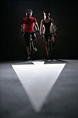 Two cyclists side by side, arrow sign on ground