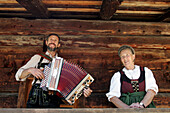 Mother and son sitting in front of log cabin, man playing Accordion, Salzburger Land, Austria