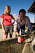 Man filling fresh water from fountain in bottle, Lammersdorfer Hütte (1650 m), Lammersdorf near Millstatt, Carinthia, Austria