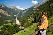 Woman looking over Heiligenblut with pilgrimage church Zum hl. Pluet to Grossglockner, Heiligenblut, Carinthia, Austria