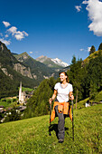 Woman hiking over alp above Heiligenblut with pilgrimage church Zum heiligen Blut, view to Grossglockner, Heiligenblut, Carinthia, Austria