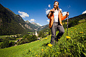 Woman hiking over alp uabove Heiligenblut with pilgrimage church Zum hl. Pluet, view to Grossglockner, Heiligenblut, Carinthia, Austria