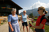 Two women with nordic walking sticks talking with Mrs. Röck, peasant woman of Amoseralm (1198 m), Dorfgastein, Gastein Valley, Salzburg, Austria