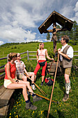 Three hikers resting at a crucifix and talking to a native man, Grossarl Valley, Salzburg, Austria