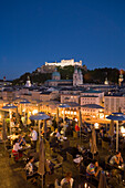View over the illuminated roof terrace of restaurant Hotel Stein in the evening, to old town with Salzburg Cathedral and Hohensalzburg Fortress the largest fully preserved fortress in central Europe, Salzburg, Salzburg, Austria