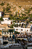 View over town in the evening, people sitting on terraces of restaurants, Lindos, Rhodes, Greece
