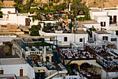 View over town in the evening, people sitting on terraces of restaurants, Lindos, Rhodes, Greece