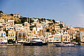 Yacht and sailing boats anchoring at quay of harbour Gialos, picturesque mansions at mountainside in background, Simi, Symi Island, Greece
