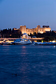 Ships and boats anchoring in Mandraki harbour (translated literally: fold) in the evening, illuminated Palace of the Grand Master and Nea Agora in background, Rhodes Town, Rhodes, Greece