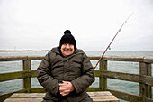 Senior man with fishing rod sitting on pear at Baltic Sea, Mecklenburg-Western Pomerania, Germany