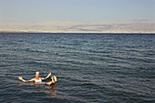 Woman bathing in the Dead Sea with Jordan in the background, Israel