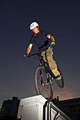 Junger Mann hüpft mit einem Trialbike auf einer Mauer, Linz, Oberösterreich, Österreich