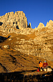Couple in front of the rock faces of Cima Brenta alta and Guglia di Brenta, Brenta Range, Italy
